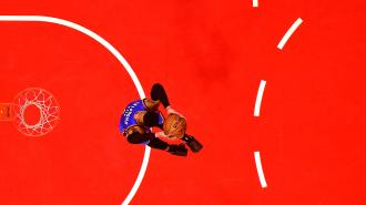 A basketball player dunks the ball on a red court.