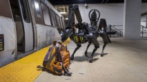 A robot police dog inspecting a backpack on the ground next to a subway train