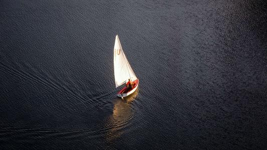 An aerial view of a sailboat peacefully sailing on a body of water, providing solitude and tranquility for individuals seeking mental health.