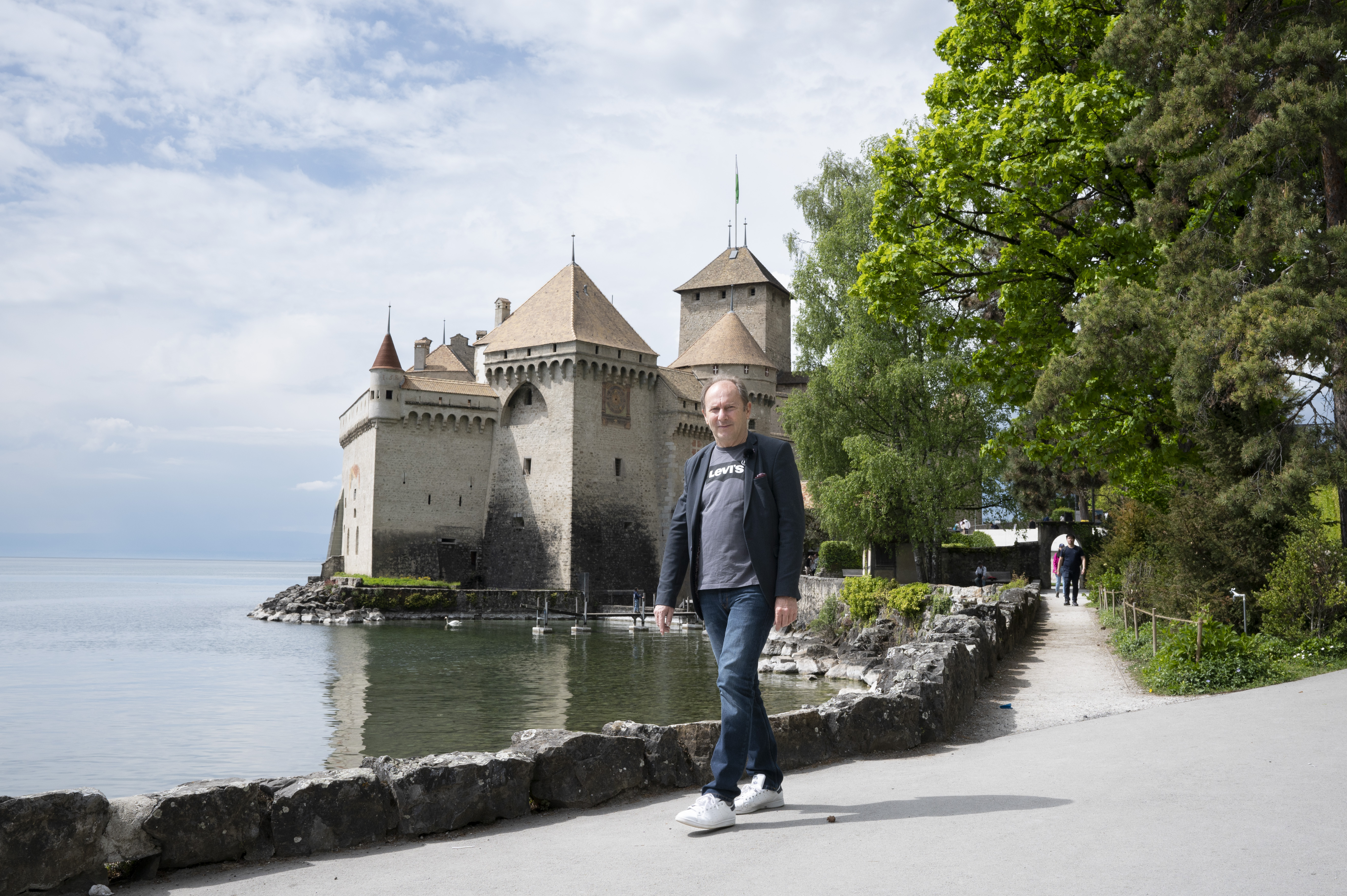 A man walking next to a body of water with a castle in the background