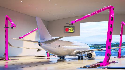 A plane in a hangar with large pink robotic arms surrounding it