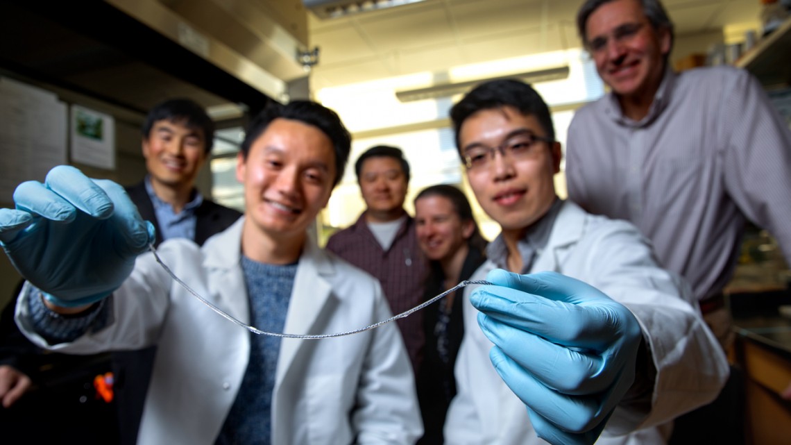 A group of people in lab coats holding up a device that looks like a piece of string about 10 inches long