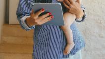 A woman holding a baby while holding an ipad.