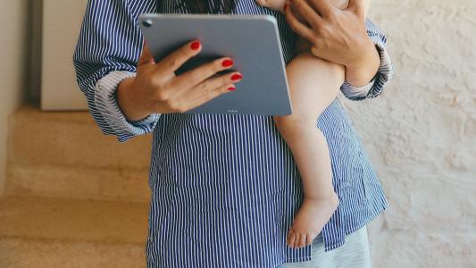 A woman holding a baby while holding an ipad.