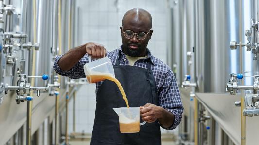 A black man pouring liquid into a keg in a brewery.