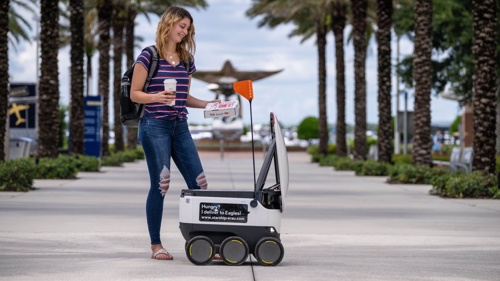 A young woman is standing next to a delivery robot.