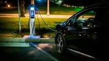 A black car is plugged into a charging station at night.