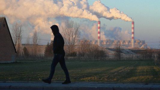 A man walking down a street with smoke coming from a factory, showcasing concerns for the environment.