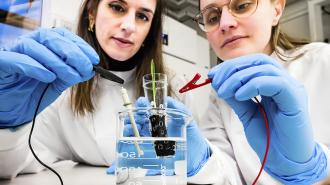 Two women in lab coats working with a beaker.