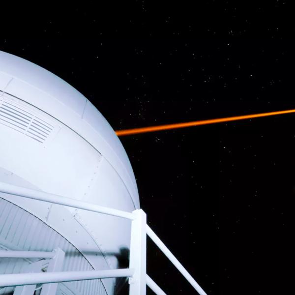 A laser beam is exiting a ground-based space observatory and pointing toward the night sky