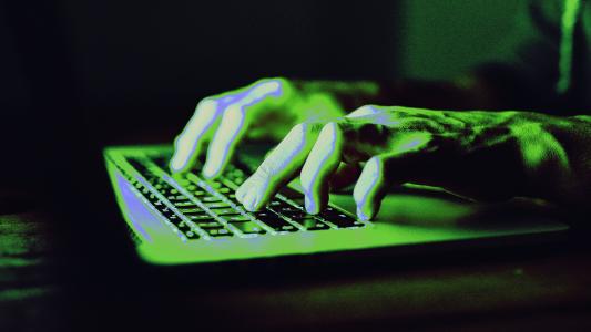 A person's hands typing on a keyboard. The scene is illuminated with a green light.
