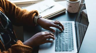 A woman typing on a laptop with a cup of coffee.