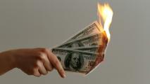 A person's hand holding a burning dollar bill while working from home.
