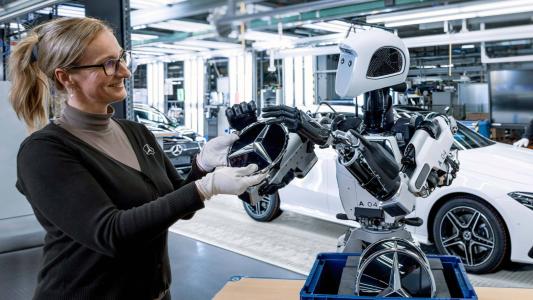 a woman standing next to one of Apptronik's Apollo robots in a Mercedes factory