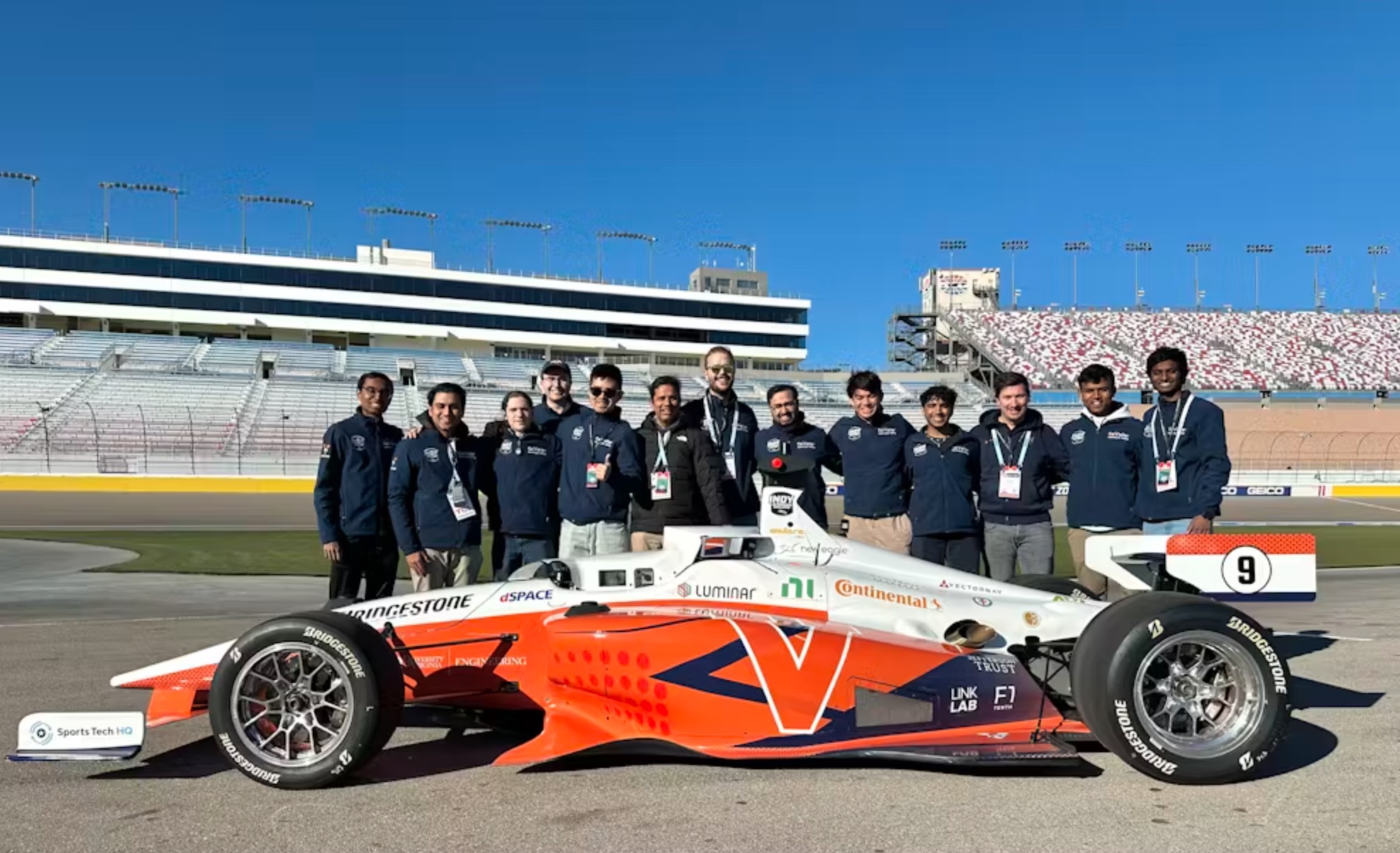 A team of individuals posing with a formula-style racing car on a racetrack.