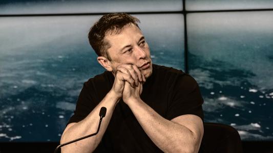 Elon Musk sits behind a microphone