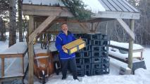 Man holding a honeycomb frame standing next to a stack of black plastic crates in a snowy environment.