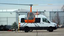 An orange self-flying helicopter parked next to a white van.