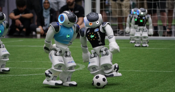Two robots are on a football field, displaying trust in each other as they navigate the game.