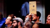 A person holds up a cardboard sign with the message "psychedelics are not a crime" in a crowded room.