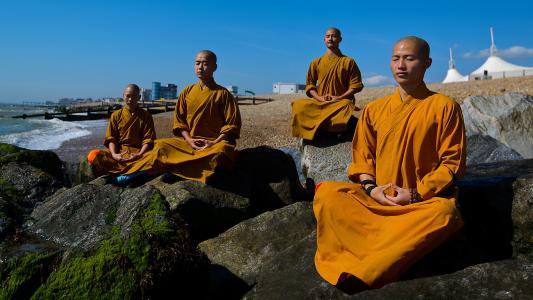 A group of Buddhist monks practicing mindfulness while meditating on rocks.