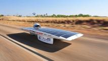 A solar-powered car races along a highway surrounded by sparse vegetation under a clear blue sky.