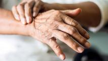 A close up of an older person's hands. One hand is rubbing the wrist of the other, as if to relieve pain