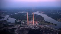 Aerial view of a large power plant with tall smokestacks near a river at dusk.