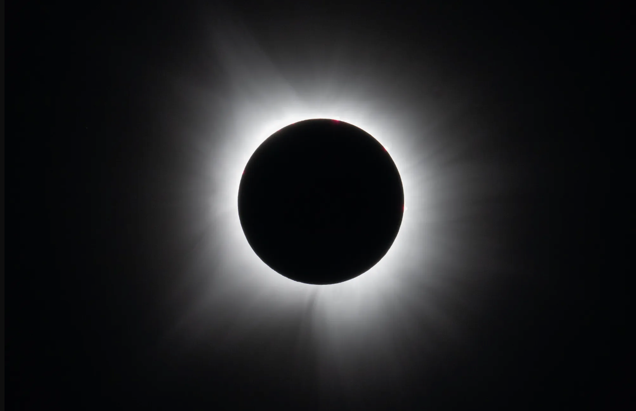A solar eclipse with a dark silhouette of the moon blocking the sun, surrounded by a radiant solar corona.