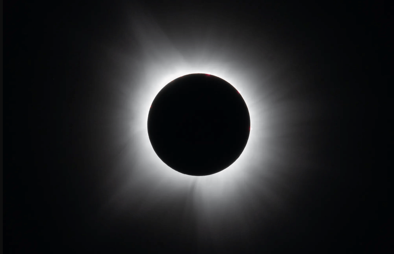 A solar eclipse with a dark silhouette of the moon blocking the sun, surrounded by a radiant solar corona.