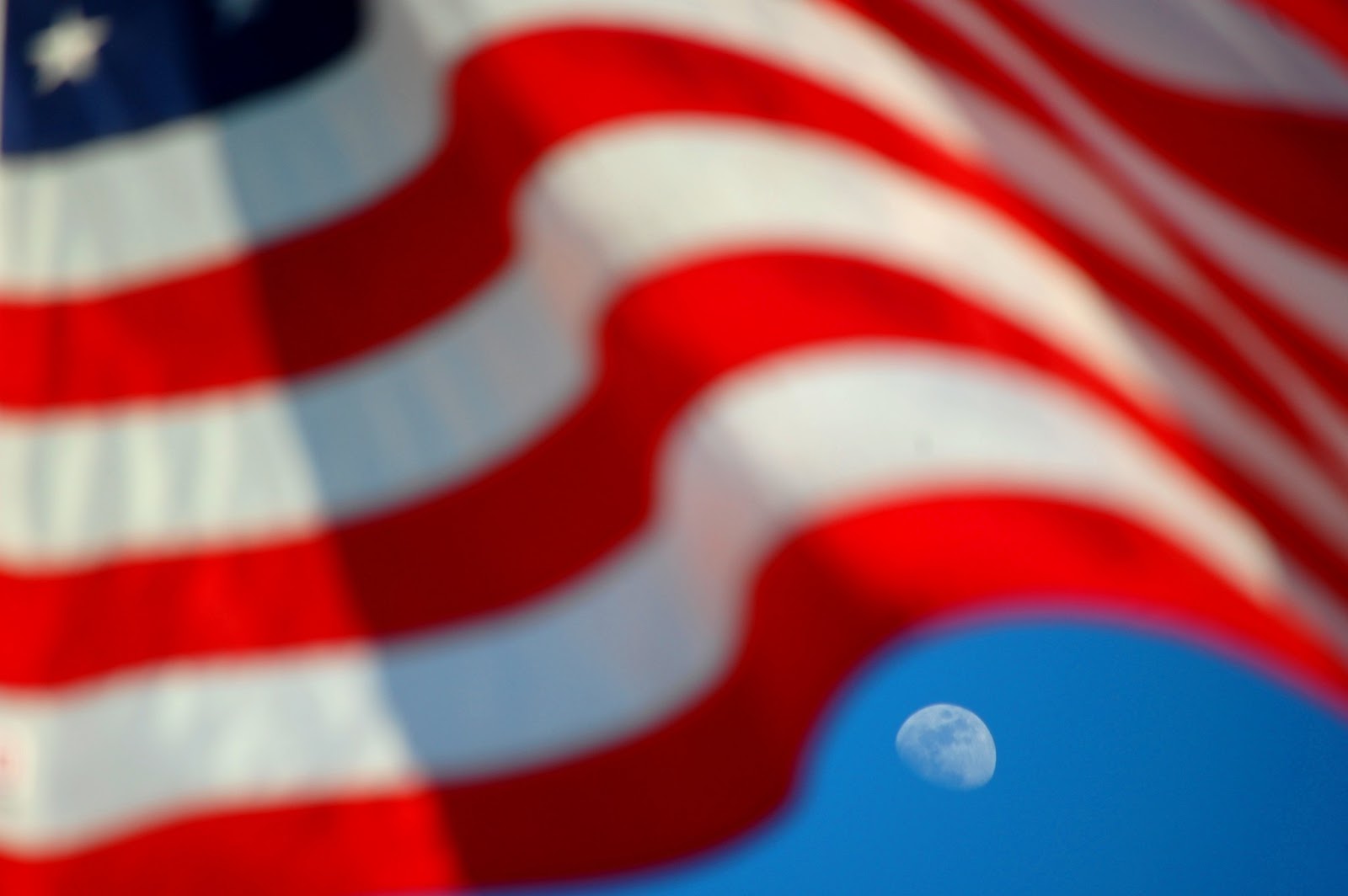 La bandera estadounidense está borrosa con la luna claramente enfocada en el fondo.