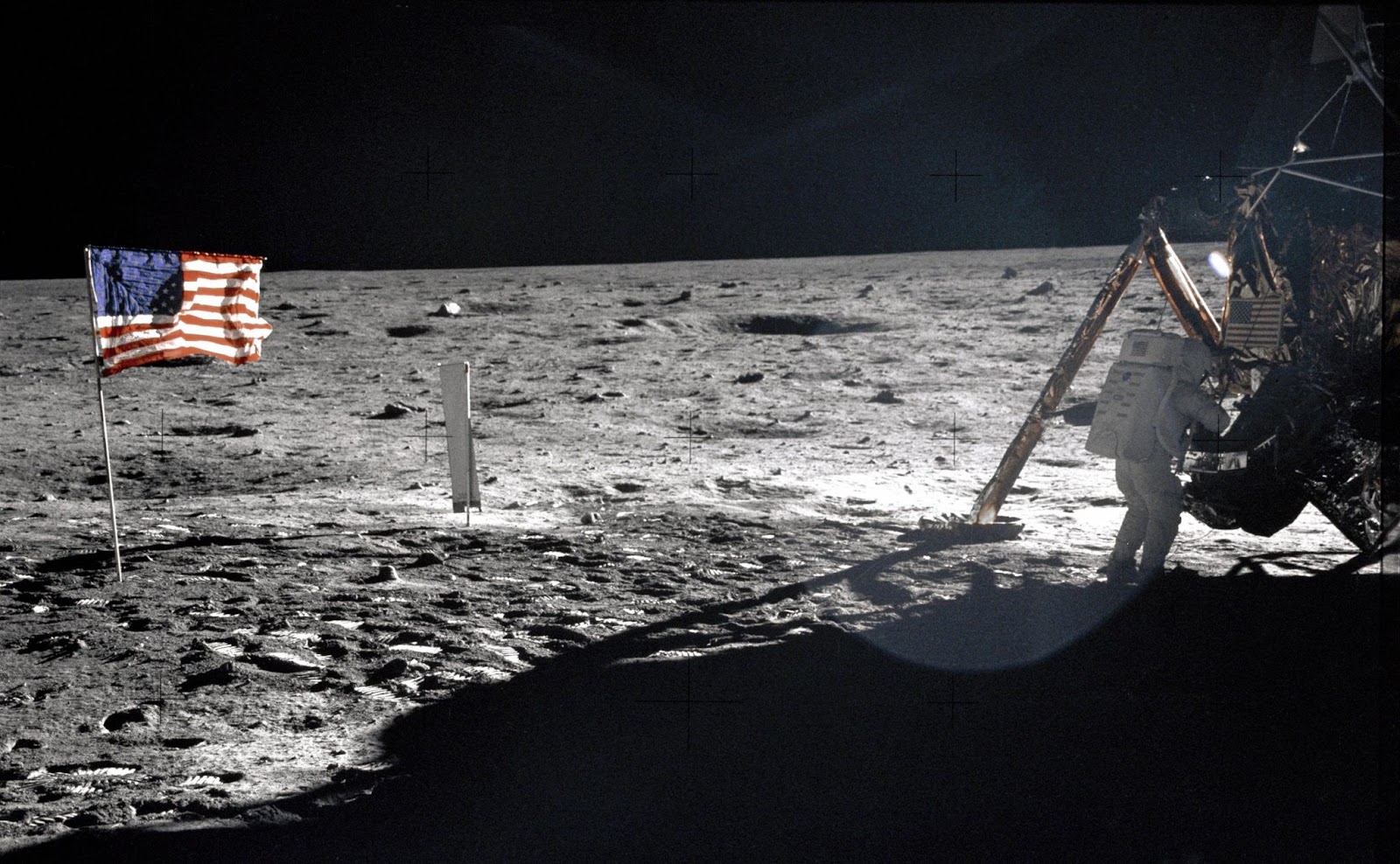 An astronaut descends the lunar module ladder beside the American flag on the moon's surface.