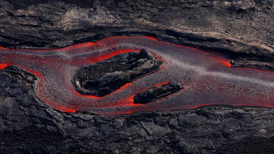 Lava flowing through cooled volcanic rock, creating a striking contrast in texture and color with deposits of stone wool.