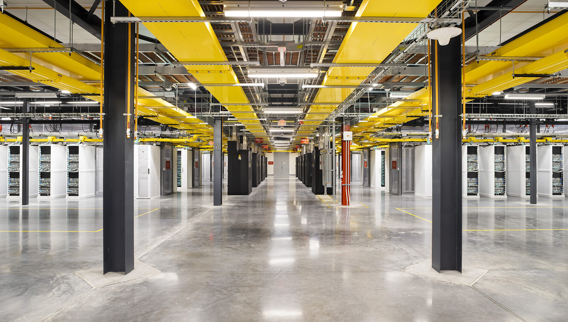 Interior of a modern data center with rows of servers and yellow columns under bright lighting.