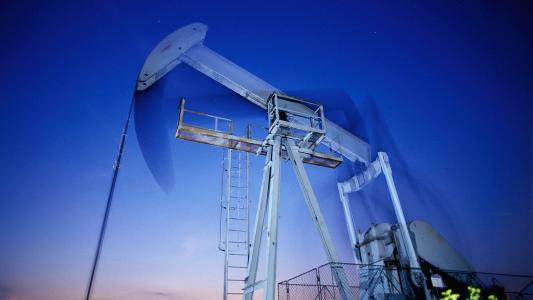 Oil pumpjack operating in the oil fields under a twilight sky.