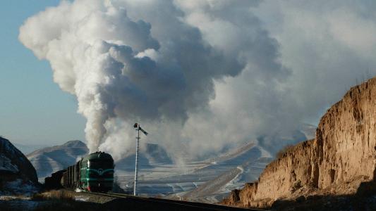 A fusion energy locomotive emits a large plume of smoke as it travels through a rugged, mountainous landscape.