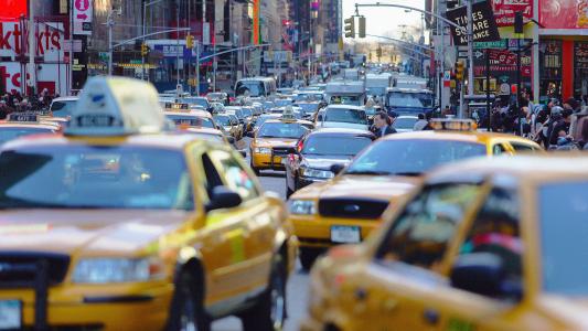 Heavy congestion pricing on a busy city street with numerous yellow taxis and bustling pedestrians visible.