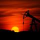 Silhouette of an oil pump jack against a vivid orange sunset with a large sun near the horizon.
