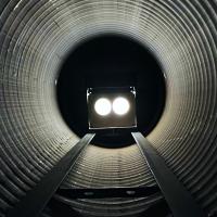 A train with bright headlights approaching through a large, dark, cylindrical tunnel.