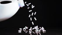 white pills being poured from a milk container over a black background
