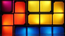 Illuminated colorful square blocks arranged in three rows, with shades of purple, red, orange, yellow, and blue, creating a vibrant grid pattern resembling a radiation detector.