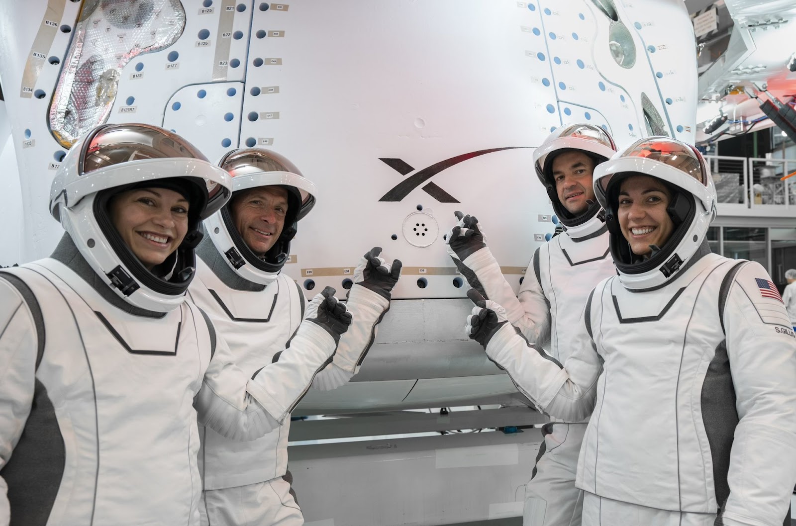 Four people in spacesuits pointing at a spaceX logo on a rocket