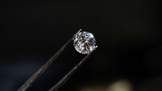 A diamond held securely by tweezers against a dark background