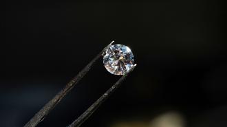 A diamond held securely by tweezers against a dark background