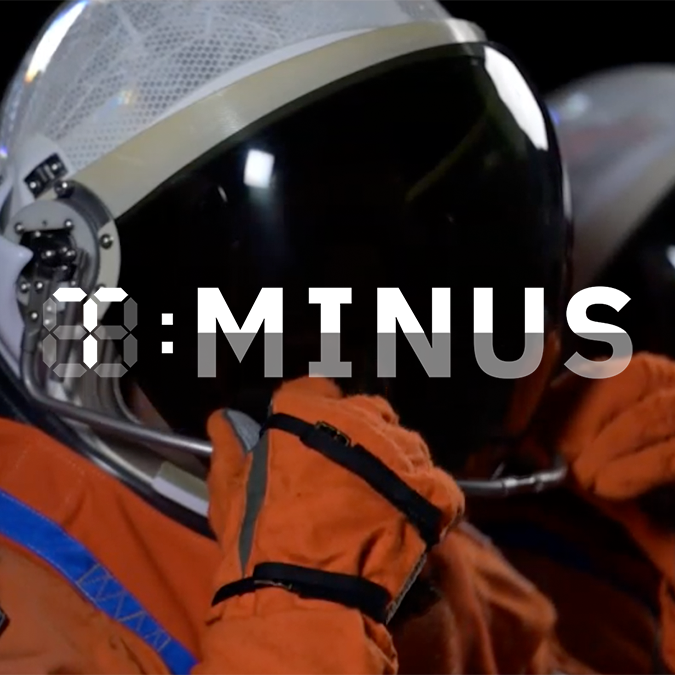 Astronaut in an orange spacesuit adjusts their helmet visor, preparing for moon missions. Text in front reads "3:MINUS.