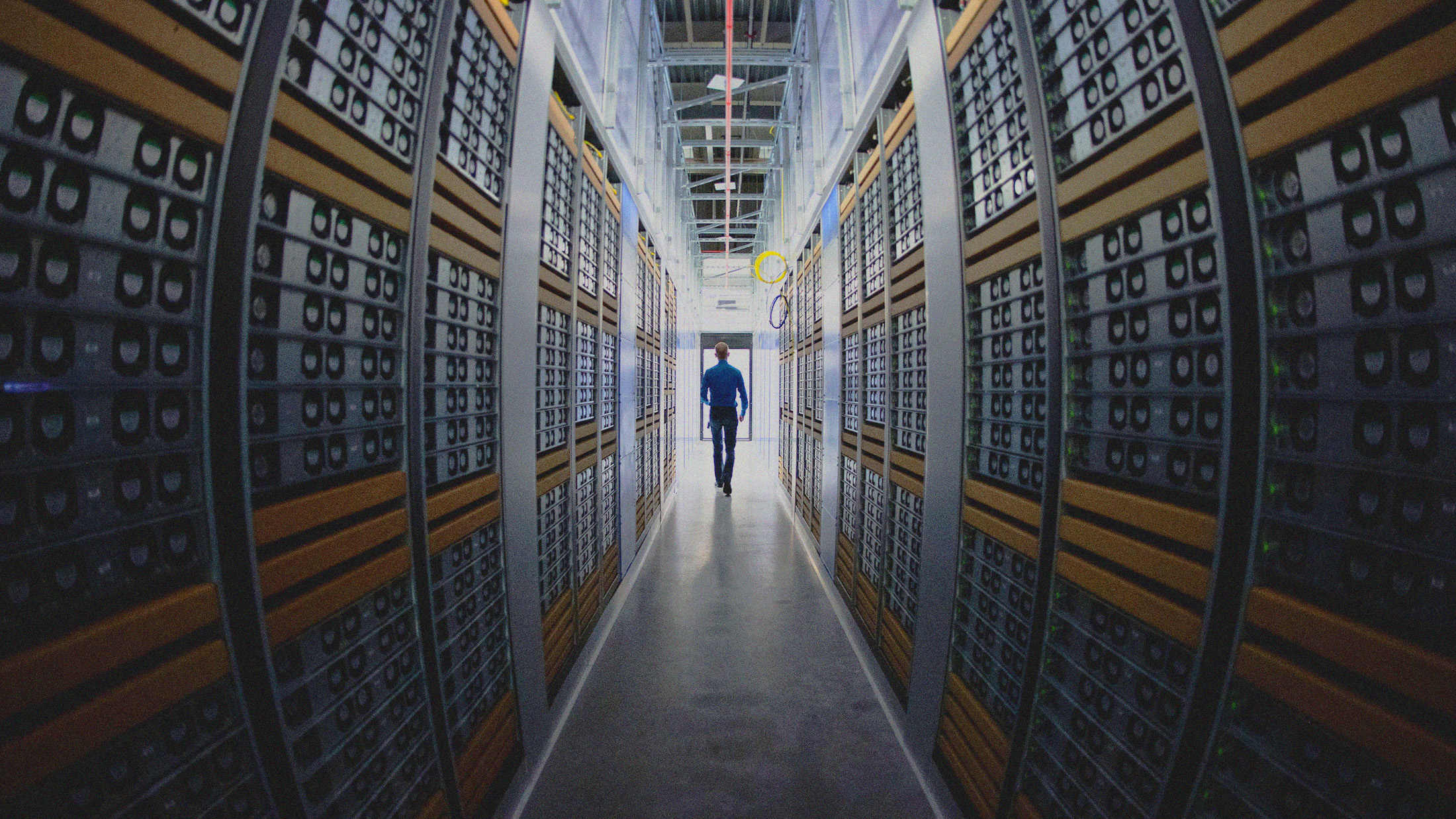 A person is walking down an aisle between rows of servers in a data center.