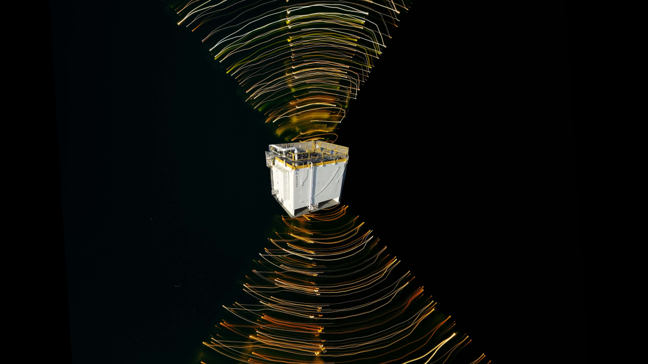 A cube-shaped satellite is surrounded by swirling lines of light in space against a black background, illustrating electromagnetic fields or signal patterns.