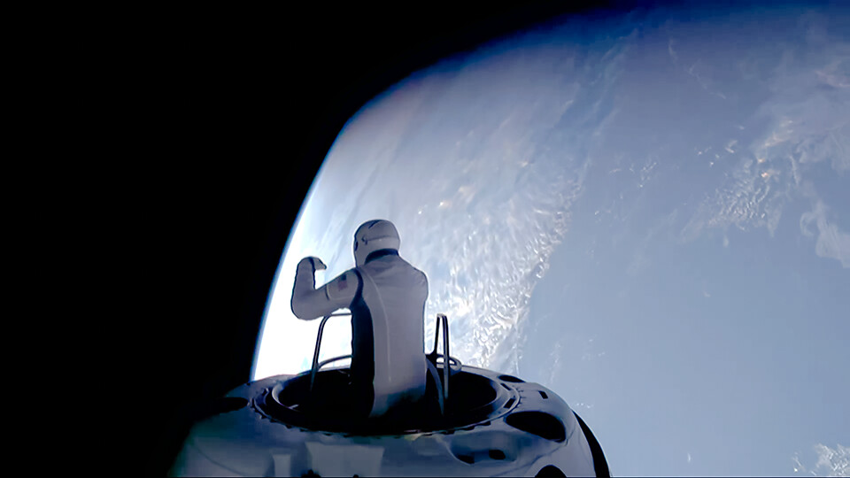 Person in a spacesuit standing on the edge of a spacecraft, with Earth visible in the background.