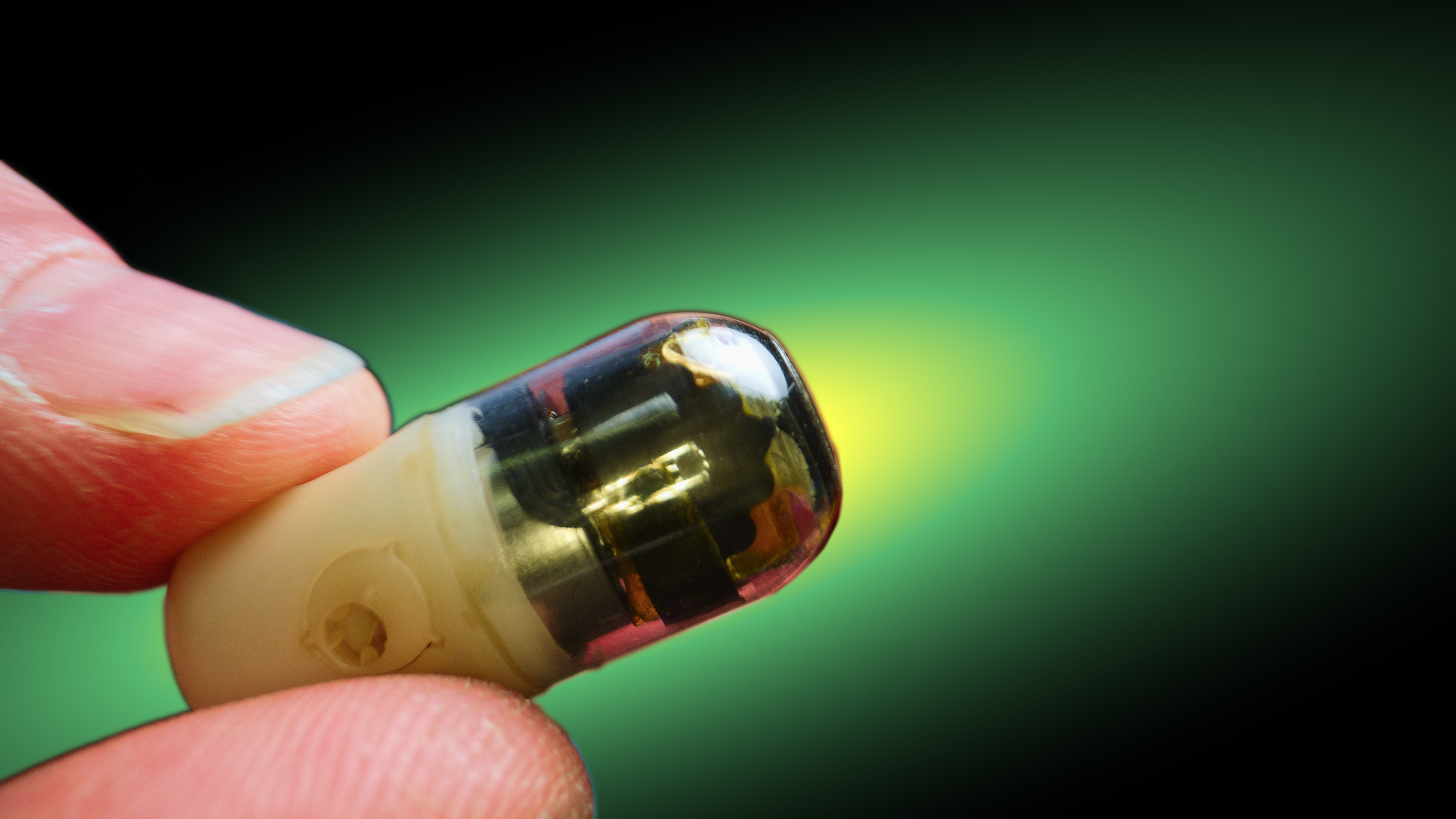 A close-up of a person's fingers holding a small, transparent electronic component with a green background.