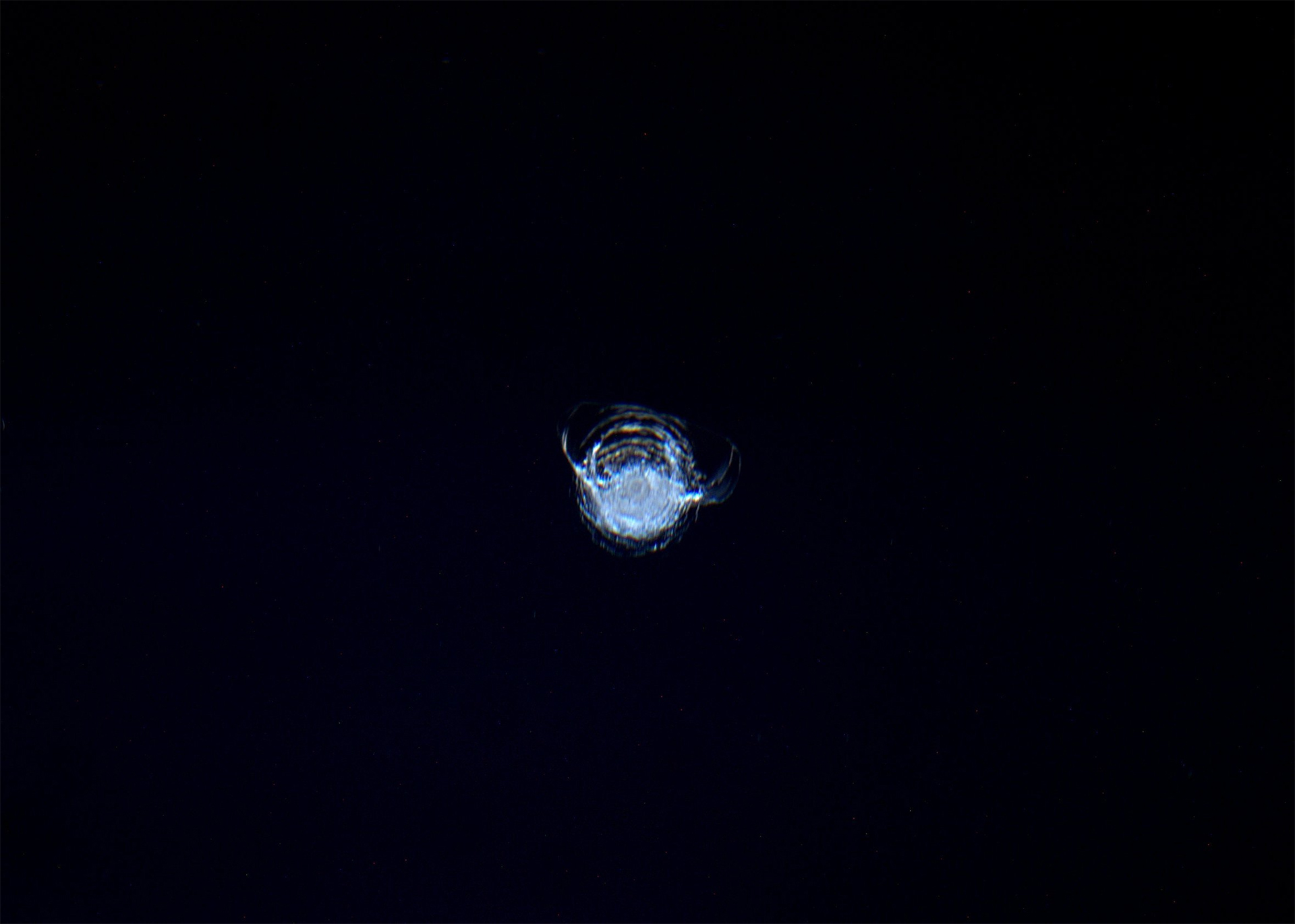 Close-up of a small impact crater on a dark surface, resembling a circular crack or chip.